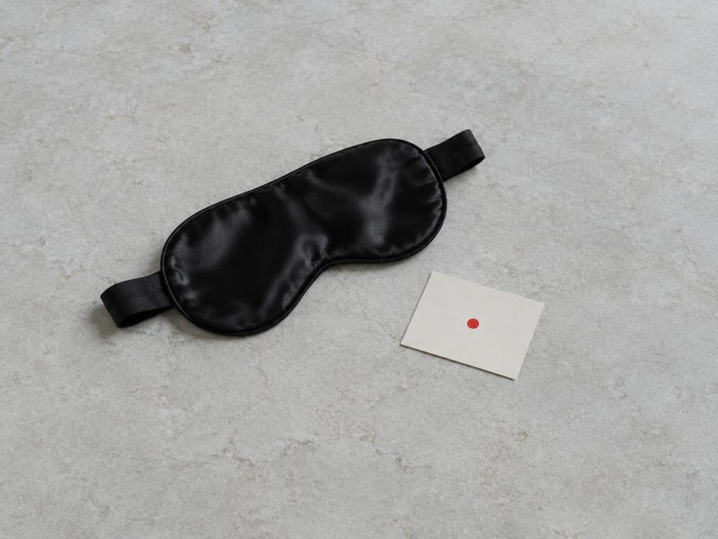 A black satin blindfold and a small card with a red dot on pale stone